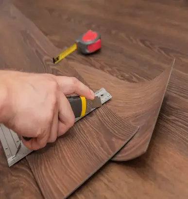 Person cutting vinyl flooring with a utility knife while fitting vinyl floors. Vinyl fitters preparing vinyl floor installation. Best vinyl flooring options in the UK.