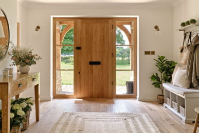 Wooden door with glass panels, a table with flowers, a bench with cushions, and plants.